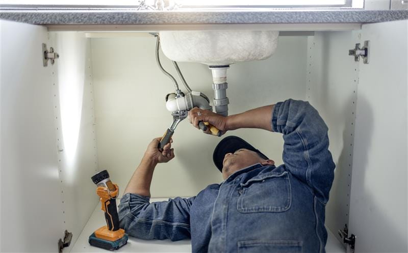 Plumber repairing pipes beneath a bathroom sink in Inglewood
